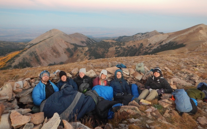A group of people sit huddled together in a desert landscape and smile for the photo.